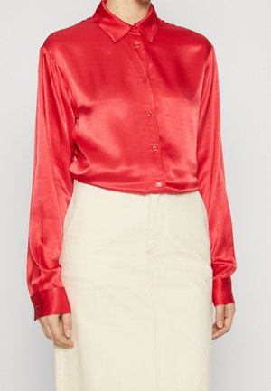 Rød satin langærmet bluse med knapper kombineret med en højtaljet off-white nederdel, vist fra skuldre til hofter mod en neutral baggrund.