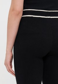 Leggings negre dintr-un material texturat, cu talie înaltă, având un accent în dungi albe în partea de sus. Croiala se conturează pe forma corpului.