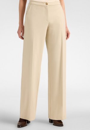 Pantaloni beige a vita alta e gamba larga con bottone frontale, tasche laterali, indossati con scarpe con tacco marrone scuro.