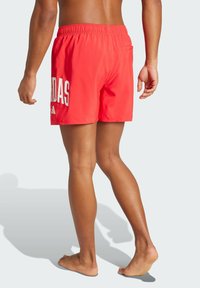 Červené plavky s bielym nápisom "ADIDAS". Elastický pás, dve bočné vrecká a hladká, ľahká tkanina.