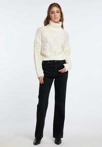 Grobstrickiger Turtleneck-Pullover mit strukturiertem Zopfmuster, kombiniert mit hoch taillierten schwarzen geraden Jeans und schwarzen Stiefeletten.