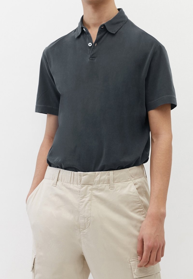 Polo-shirt court gris foncé à manches courtes avec un col, patte de boutonnage à deux boutons, texture douce, associé à un pantalon cargo beige avec poches latérales.