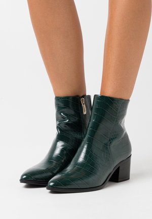 Green crocodile-embossed ankle boots with a glossy finish, pointed toes, and a low block heel. Features a side zipper for closure.