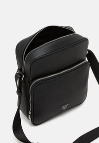 Sac en cuir noir porté crossbody avec deux compartiments zippés, une texture lisse et des accents en métal argenté. Bandoulière réglable incluse.