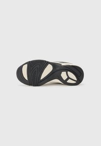 Semelle de sneaker noire et beige avec un caoutchouc texturé, présentant un motif en vague, des rainures pour l'adhérence et un design global épuré.