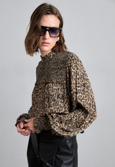 Leopardimustriline blouse smockitud kaelusega, pikkade varrukatega ja kogutud mansettidega, valmistatud kergest kangast; kantud mustade nahkpükstega.