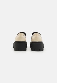 Beige bőr cipők vastag fekete gumitalppal, slip-on kialakítással és látható varrási részletekkel a felsőrészen.