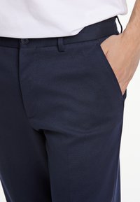 Pantalones navales confeccionados con una tela suave, con un diseño de frente plano, bolsillos laterales y una silueta ajustada con cierre de botón.