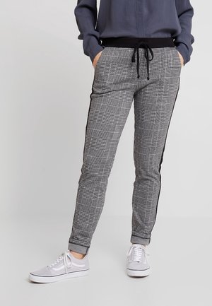 Pantalons à carreaux noir et blanc avec taille élastique, cordon de serrage, et rayures d'accent sur les côtés ; associés à des baskets grises.
