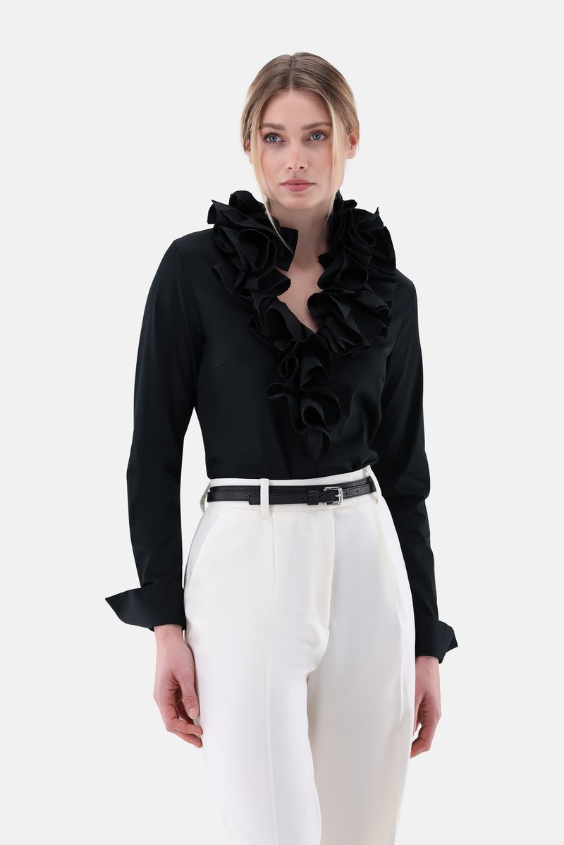Black blouse with a ruffled collar, long sleeves, and cuffs. Paired with white trousers and a black belt. Smooth fabric, tailored fit.