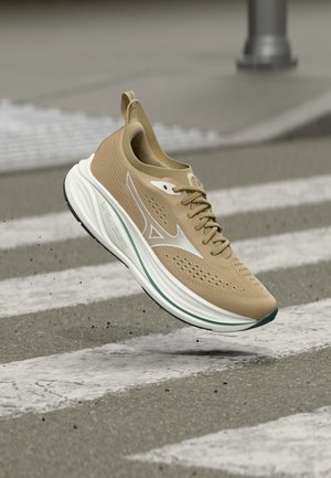 Hellbrauner Sportschuh mit weißer Sohle und Logo, schwebt in der Luft über einem Zebrastreifen mit Asphaltboden.