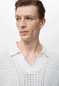 Polo shirt bianco a maglia con un motivo testurizzato, scollatura a V e colletto corto, con dettagli a punto aperto su tutta la stoffa.