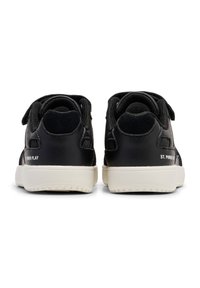 Zapatillas negras de cuero con correas de velcro, acentos texturizados y una suela de goma blanca. Presenta texto impreso en el talón.