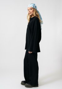Completo in tessuto a coste nero con pantaloni a gamba larga e una maglia oversize. Accentato con un foulard a righe blu chiaro e scarpe nere chunky.