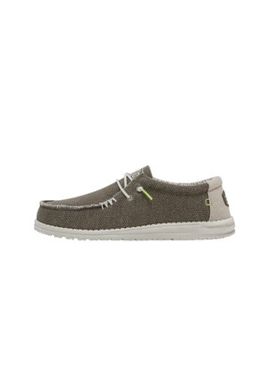 Chaussure slip-on décontractée en tissu olive texturé, semelle blanche, lacets blancs, pièce claire au talon et petit accent vert sur le côté.