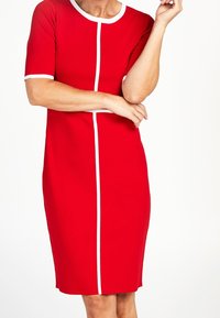 Abito rosso realizzato in tessuto elastico, con maniche corte, scollatura rotonda e linee bianche che decorano verticalmente la parte anteriore.
