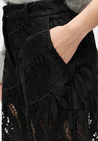 Pantalon en dentelle noire avec des motifs floraux complexes et une poche latérale, doté d'une texture douce et d'une coupe ajustée.