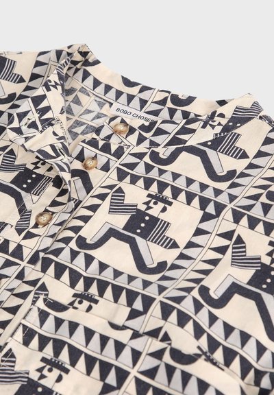 Camicia con motivo geometrico in bianco e nero che presenta figure stilizzate di corsa che indossano cappelli, chiusura frontale con bottoni e una piccola tasca sul petto.
