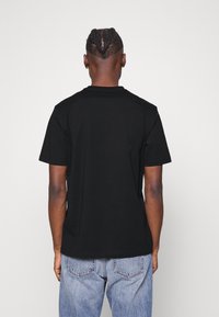 T-shirt nera in cotone con scollo rotondo e maniche corte, vista dal retro. Tessuto testurizzato con una vestibilità rilassata.