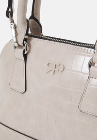 Ljust beige handväska med krokodilmönster, silverfärgad hårdvara och ett översta blixtlås. Har en framträdande logotyp på framsidan och kontrasterande kant.