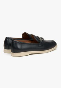 Leren loafers in marineblauw met een gladde afwerking, voorzien van een decoratieve zilveren accent en een contrasterende beige rubberen zool.