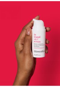 Weißer Pumpbehälter mit rotem Text, gefüllt mit einem Vitamin C Serum, in einer Hand gegen einen hellpink Hintergrund gehalten. Größe 30ml.