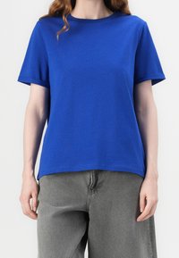Blue crew neck t-shirt made of cotton, featuring short sleeves and a relaxed fit. Paired with loose-fitting gray pants, with a smooth texture.