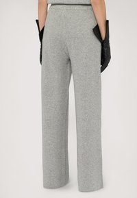 Szare, żebrowane spodnie damskie z szerokimi nogawkami i wysokim stanem. Zawierają boczne kieszenie i są zestawione z czarnymi skórzanymi rękawiczkami, co podkreśla kontrast.