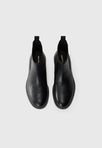 Bottines en cuir noir avec une texture lisse et des panneaux latéraux élastiques. Équipées d'une languette pour unEnfilage facile. Marque Geox visible à l'intérieur.