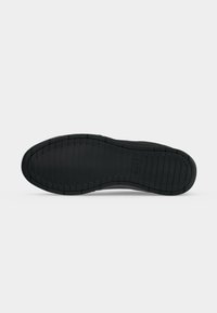 Semelle de chaussure noire avec des rainures horizontales et le nom de la marque "BOSS" embossé près du centre de la semelle.