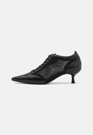Shoe preto de bico fino com um design de painel em malha, apresentando um salto baixo e amarração na parte da frente. Feito de uma combinação de couro e material de malha.