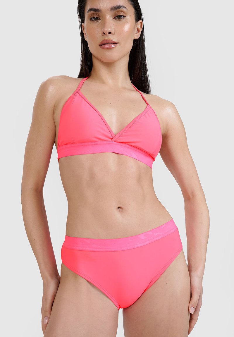Femme portant un haut de bikini rose vif à col halter et un bas de bikini taille haute assorti sur un fond uni.