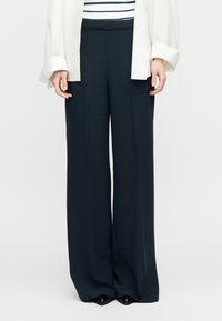 Παντελόνια με φαρδιά μπατζάκια σε σκουρο μπλε ναυτικό χρώμα με λεία υφή, ραμμένη σχεδίαση και ψηλή μέση, συνδυασμένα με λευκό πουκάμισο και ριγέ τοπ από κάτω.