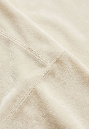 Nahaufnahme eines weichen beigen Stoffs mit einer doppelt abgesteppten Naht, die diagonal über die Oberfläche verläuft.