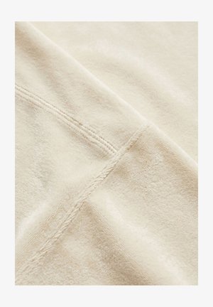 Nahaufnahme eines weichen beigen Stoffs mit einer doppelt abgesteppten Naht, die diagonal über die Oberfläche verläuft.