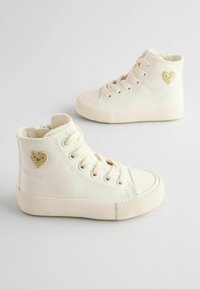 Sneakers alte bianche in tela con suola in gomma testurizzata, caratterizzate da un ricamo a forma di cuore dorato sul lato esterno. Lacci piatti e puntale circolare.
