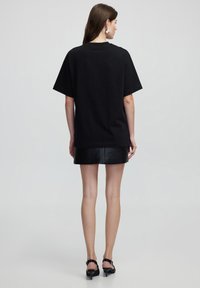 Zwart oversized t-shirt met korte mouwen, gemaakt van katoen. Gladde textuur. Gecombineerd met een zwarte leren minirok en hoge sandalen.