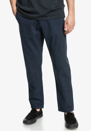 Hosen mit navy-blauen Streifen aus einem strukturierten Stoff, mit einem lässigen Schnitt und Seitentaschen, kombiniert mit schwarzen Slippers.