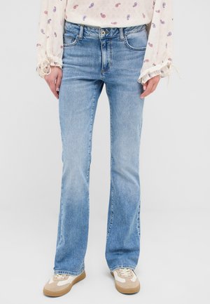 Light blue flared jeans with a faded wash, five-pocket design, and metal hardware. Paired with beige and white sneakers.