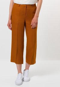 Pantalon marron à jambes larges en tissu léger, avec une texture lisse et une coupe taille haute, associé à des baskets blanches.
