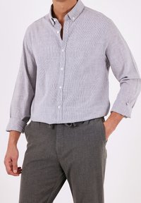 Ljusgrå skjorta med knappar och ett strukturerat mönster, uppvikta ärmar och en klassisk krage, i kombination med mörkgrå byxor med elastisk midja.