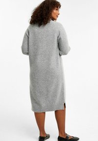 Grau gestricktes Kleid mit lässiger Passform, seitlichen Schlitzen und gerippten Säumen. Weicher Stoff mit Dreiviertelärmeln und wadenlanger Länge.
