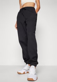 Svart bomullssweatpants med snøring i midjen og elastiske mansjetter, utstyrt med sidelommer og en liten logo på venstre lår.