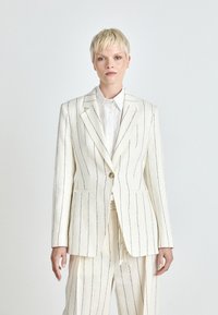 Off-white gestreept pak met een op maat gemaakte blazer en bijpassende broek. De blazer heeft twee zakken en een enkele knoopsluiting. Glad textuur.