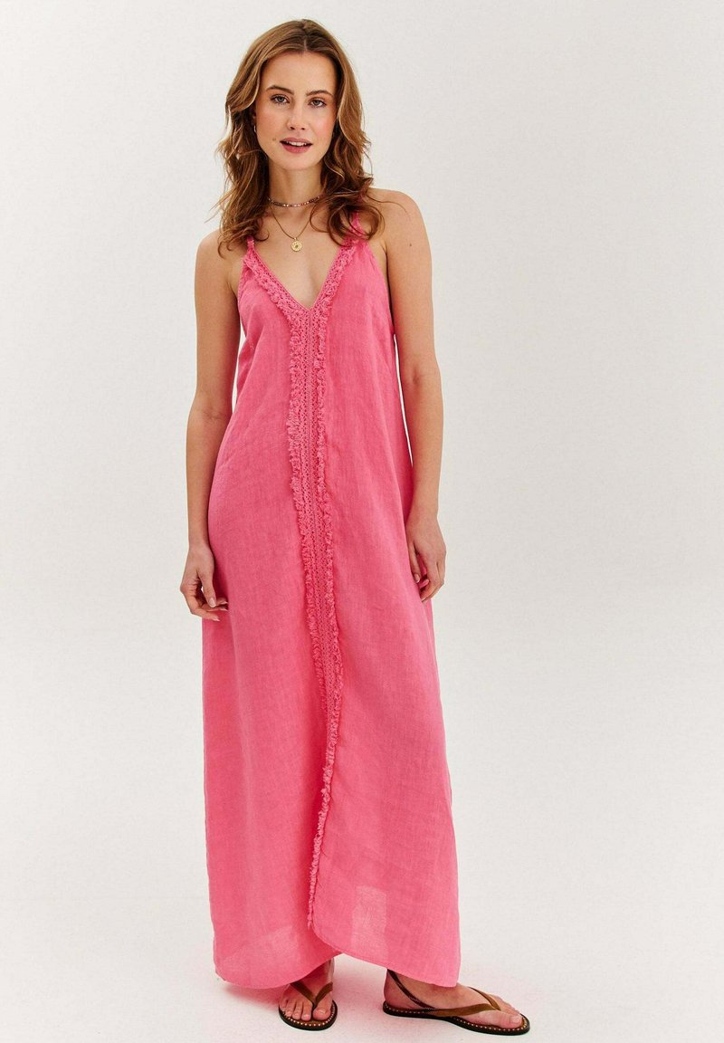 Ružová maxi šaty z ľanu s V-výstrihom, zdobené riasením vpredu a tenkými ramienkami. V páre s hnedými šľapkami. Ľahká, vzdušná textúra.