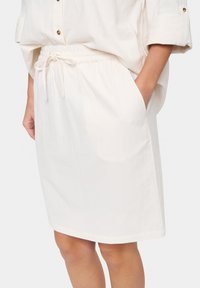 Dragsko kjol i off-white tyg. Har en elastisk midja, sidofickor och en rak silhuett med en fåll som sitter precis ovanför knäna.