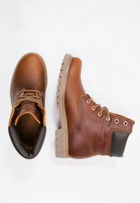 Bottines en cuir marron avec une semelle en caoutchouc, une semelle de traction beige clair, des lacets marron et un col de talon noir contrastant.