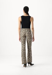 Crna bezrukavna majica u kombinaciji s trapericama u leopard printu, koje imaju bež pozadinu s crnim mrljama i glatkom teksturom. Crne štikle.