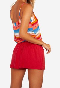 Top sin mangas a rayas de múltiples colores con pantalones cortos rojos. Tejido ligero, ajuste relajado, con una cintura fruncida y botones decorativos en los pantalones cortos.