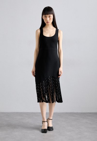 Schwarz Kleid mit Rundhalsausschnitt, tailliertem Oberteil und fransigem Saum. Die Fransen sind mit Pailletten verziert. Kombiniert mit schwarzen Riemchen-Heels.